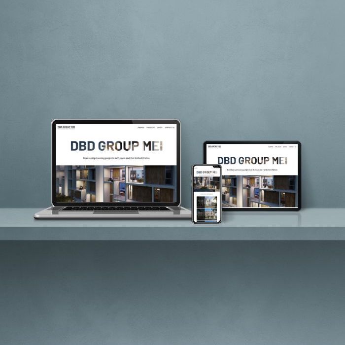 Electronic devices including laptop, tablet, and phone neatly arranged on a table, each showing the homepage of the DBD Group MEI website.