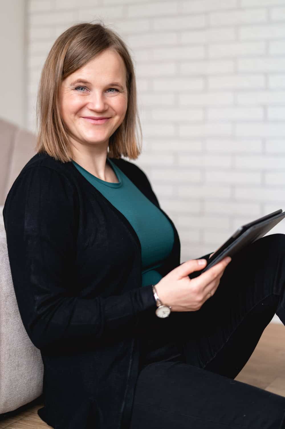 Barbora sitting on a couch holding a tablet and smiling.